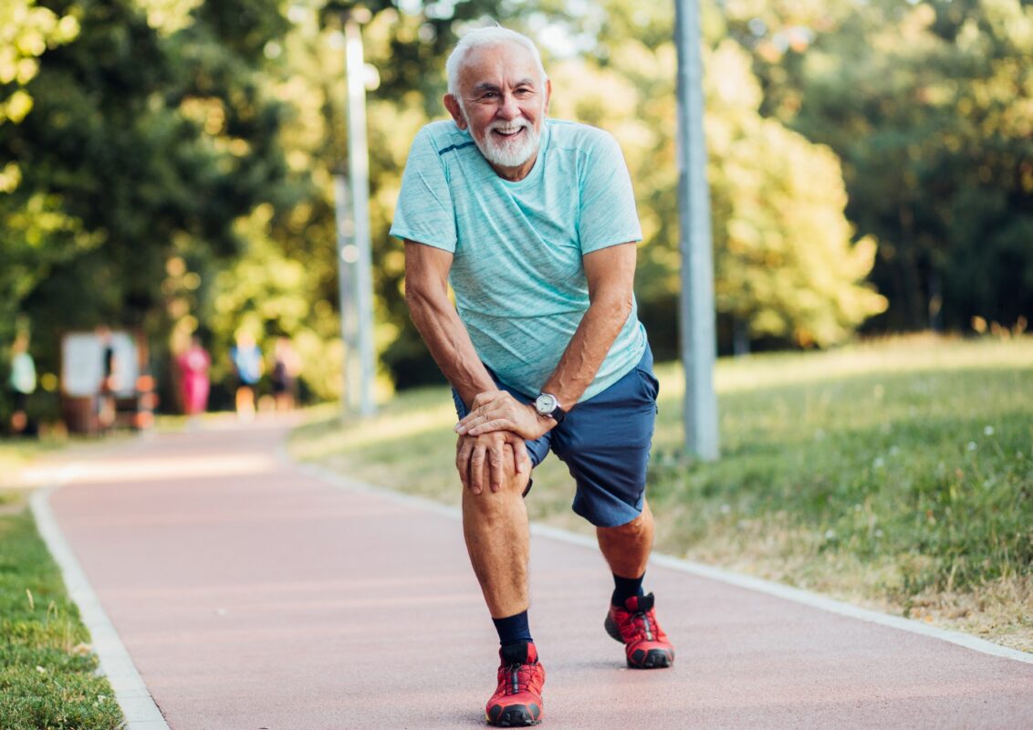 Una persona mayor, con una sonrisa en el rostro, trotando o caminando en un parque soleado, transmitiendo energía y bienestar. Podría estar acompañada de otra persona o sola, mostrando que la actividad física es posible y agradable en la tercera edad.