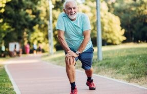 Una persona mayor, con una sonrisa en el rostro, trotando o caminando en un parque soleado, transmitiendo energía y bienestar. Podría estar acompañada de otra persona o sola, mostrando que la actividad física es posible y agradable en la tercera edad.