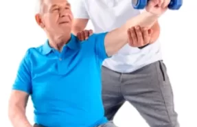 Kinesiólogo ayudando a un paciente a realizar un ejercicio terapéutico en el salón de su casa, ilustrando la atención personalizada y el entorno cómodo de la kinesiología a domicilio.