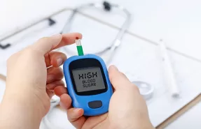Primer plano de una persona utilizando un glucómetro para medir su nivel de azúcar en sangre, representando la importancia del control y la prevención de la diabetes.