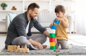 Padre jugando con su hijo en casa con juguetes educativos sobre una alfombra.