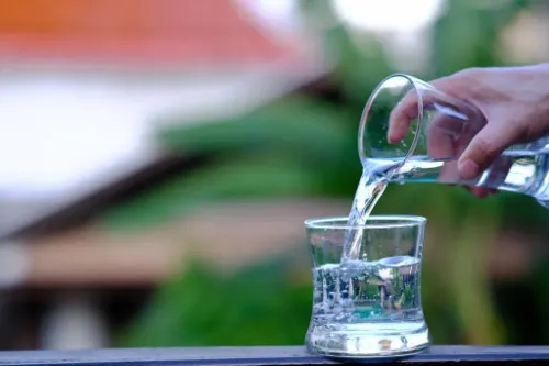 Vaso de agua pura junto a frutas hidratantes, representando los beneficios del agua para el cuerpo y el bienestar.